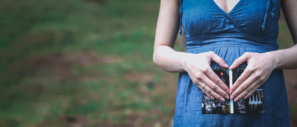 Pregnant woman holding an ultrasound image in front of her body